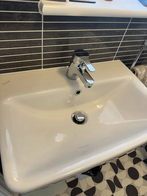 Pristine white bathroom basin with chrome tap on dark grey tile splashback, cleaned by True Grit Cleaning Co for an Airbnb changeover